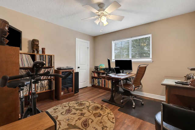 home office featuring a ceiling fan, a textured ceiling, baseboards, and wood finished floors