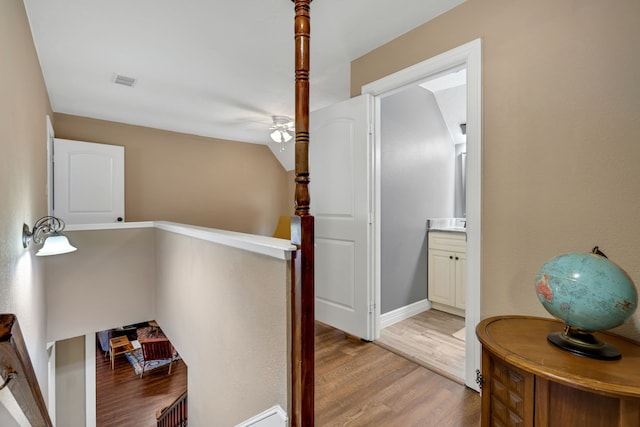 corridor with visible vents, light wood-type flooring, an upstairs landing, and baseboards