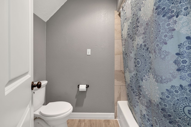 bathroom with baseboards, a textured wall, toilet, wood finished floors, and shower / bath combination with curtain