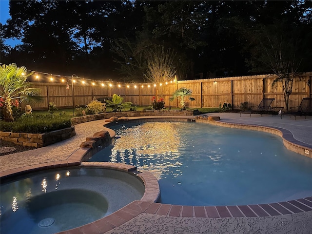 pool at night featuring a fenced backyard, a pool with connected hot tub, and a patio