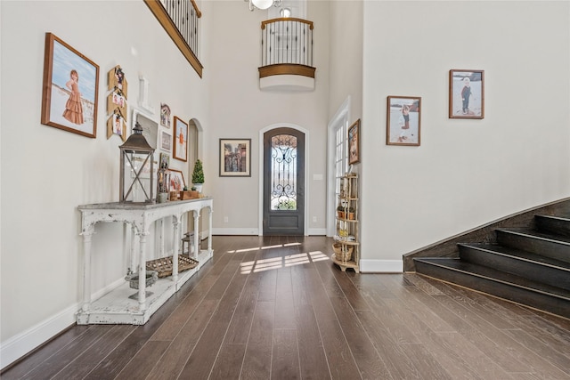 foyer with arched walkways, a high ceiling, wood finished floors, baseboards, and stairs