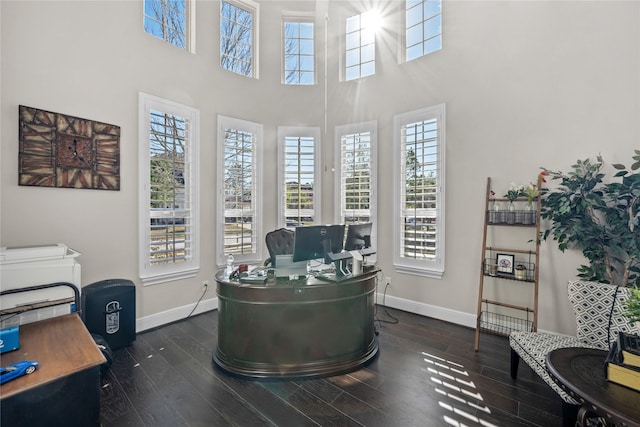 office space featuring dark wood-style flooring, a towering ceiling, and baseboards