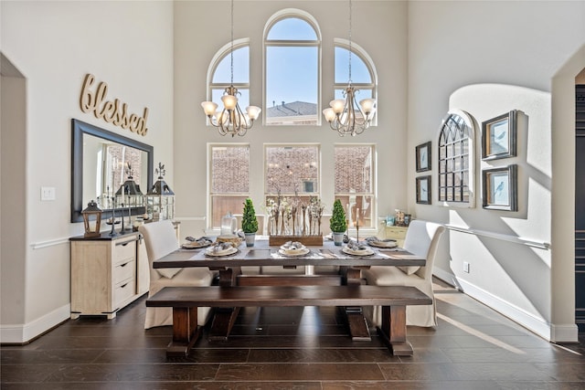 dining area with a chandelier, dark wood-style flooring, a towering ceiling, and baseboards