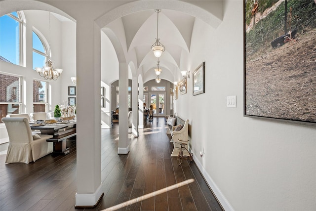 entrance foyer with arched walkways, a notable chandelier, dark wood-style flooring, a towering ceiling, and baseboards