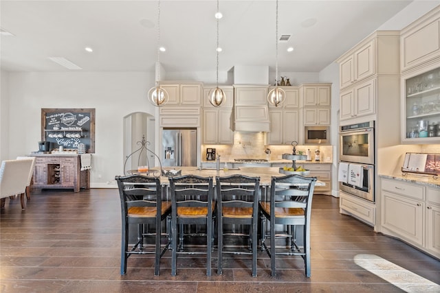 kitchen with light stone counters, arched walkways, backsplash, cream cabinets, and appliances with stainless steel finishes