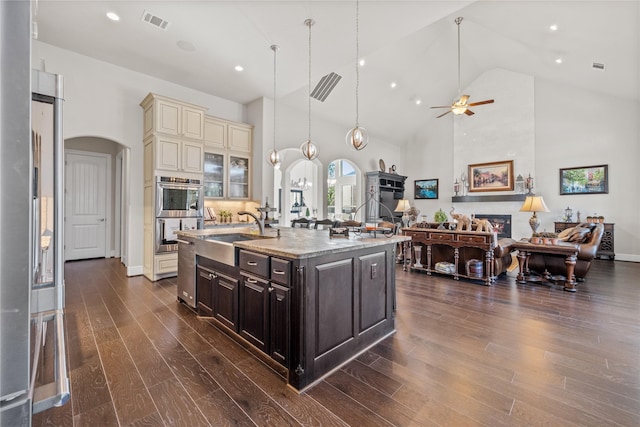 kitchen with a large fireplace, visible vents, arched walkways, cream cabinets, and a sink