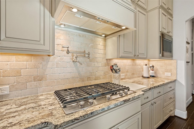 kitchen with light stone counters, backsplash, cream cabinets, appliances with stainless steel finishes, and extractor fan