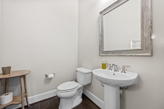 half bath with toilet, baseboards, and wood finished floors