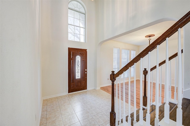 foyer entrance featuring arched walkways, stairway, a towering ceiling, light tile patterned flooring, and baseboards