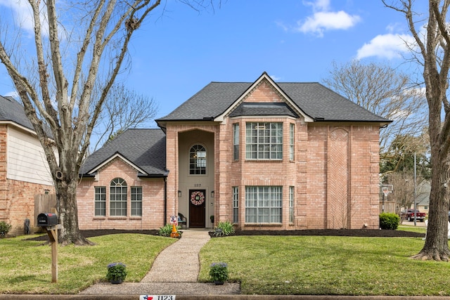 traditional-style home featuring roof with shingles, a front lawn, and brick siding