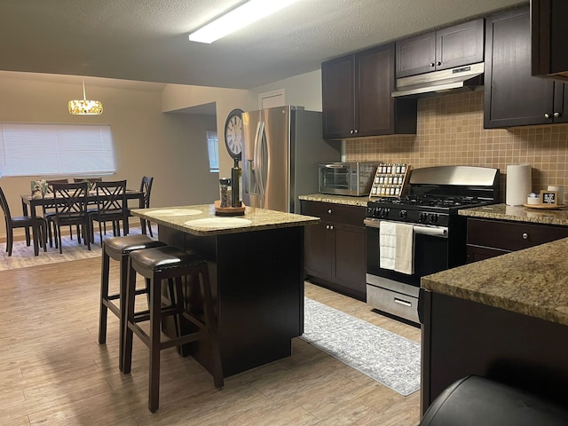 kitchen featuring stainless steel appliances, light wood-type flooring, under cabinet range hood, and decorative backsplash