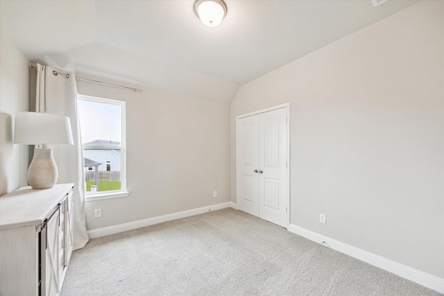 unfurnished bedroom featuring a closet, light colored carpet, baseboards, and vaulted ceiling