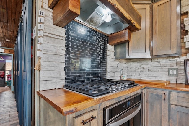 kitchen featuring stainless steel appliances, butcher block counters, backsplash, and wall chimney range hood