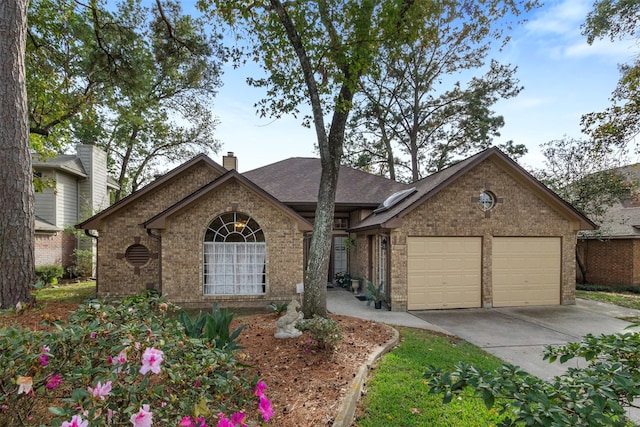 view of front of house with brick siding, a chimney, a shingled roof, a garage, and driveway