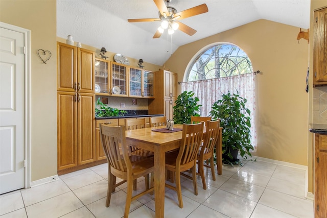 dining room featuring a ceiling fan, lofted ceiling, baseboards, and light tile patterned floors