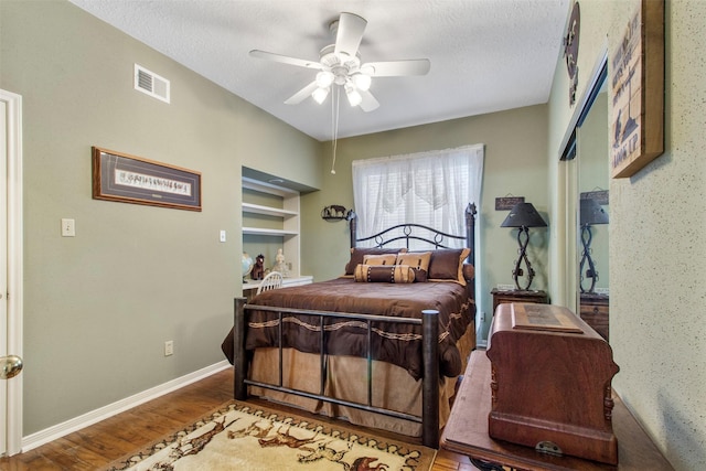 bedroom featuring a textured ceiling, wood finished floors, visible vents, and baseboards