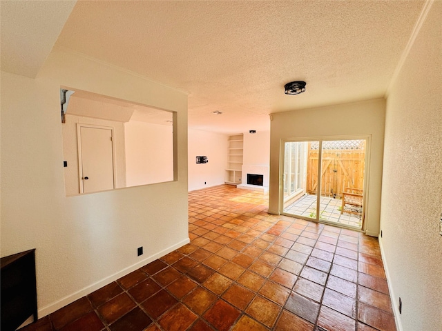 empty room with baseboards, a fireplace with raised hearth, a textured wall, a textured ceiling, and built in shelves