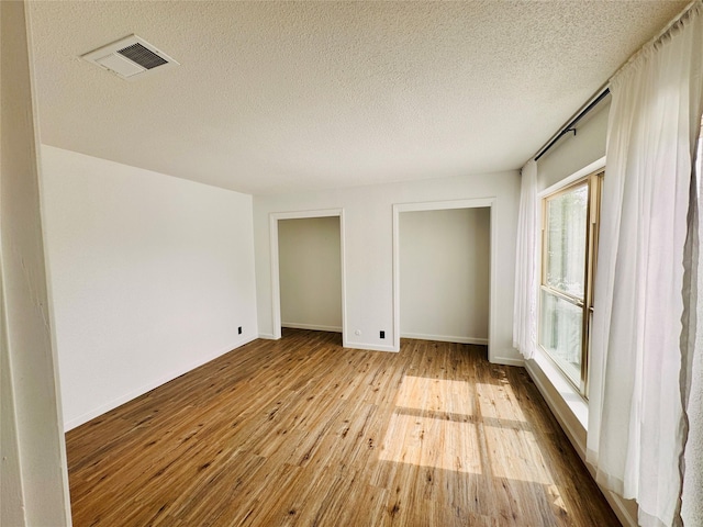 spare room with visible vents, a textured ceiling, baseboards, and hardwood / wood-style flooring