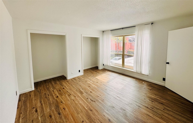 unfurnished bedroom featuring a textured ceiling, wood finished floors, and baseboards