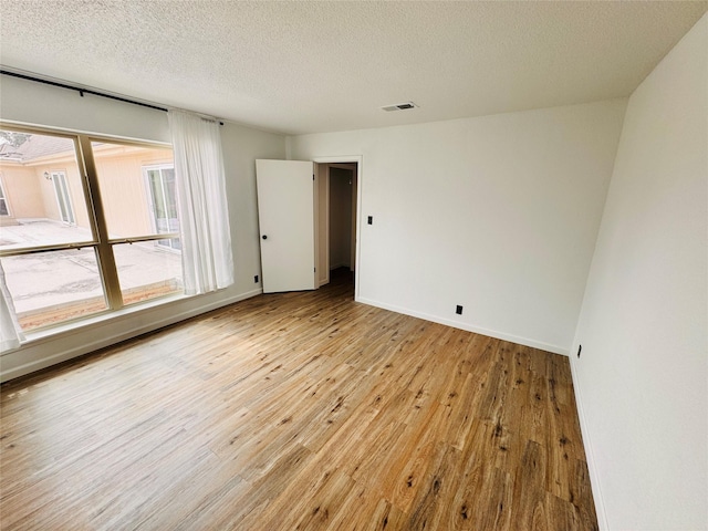 spare room with baseboards, visible vents, a textured ceiling, and hardwood / wood-style floors