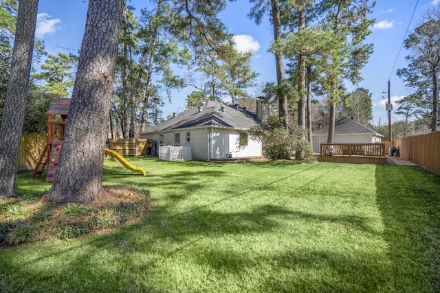 view of yard featuring a deck, a playground, and a fenced backyard