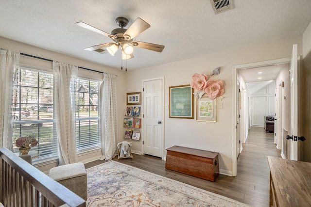 living area featuring visible vents, a ceiling fan, a textured ceiling, wood finished floors, and baseboards