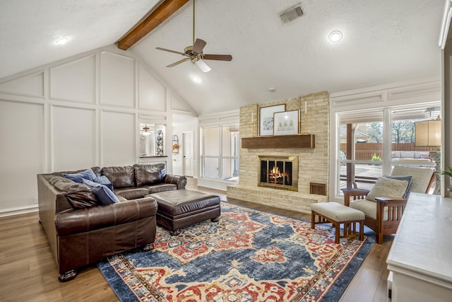 living area featuring beamed ceiling, a fireplace, visible vents, and a decorative wall