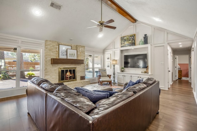 living room featuring high vaulted ceiling, a fireplace, wood finished floors, visible vents, and beam ceiling