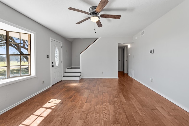 unfurnished living room featuring baseboards, visible vents, stairway, and wood finished floors