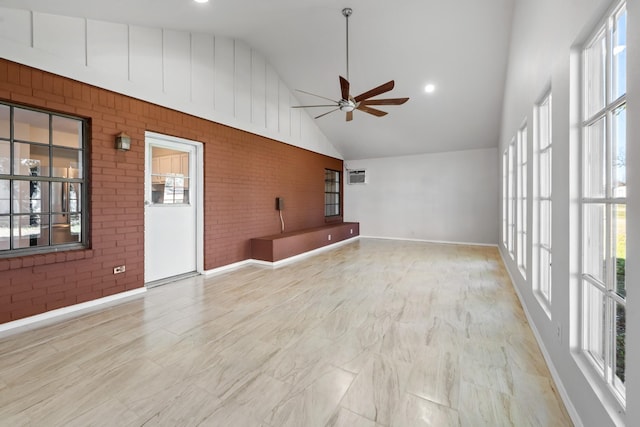 empty room featuring a ceiling fan, brick wall, high vaulted ceiling, and a wealth of natural light