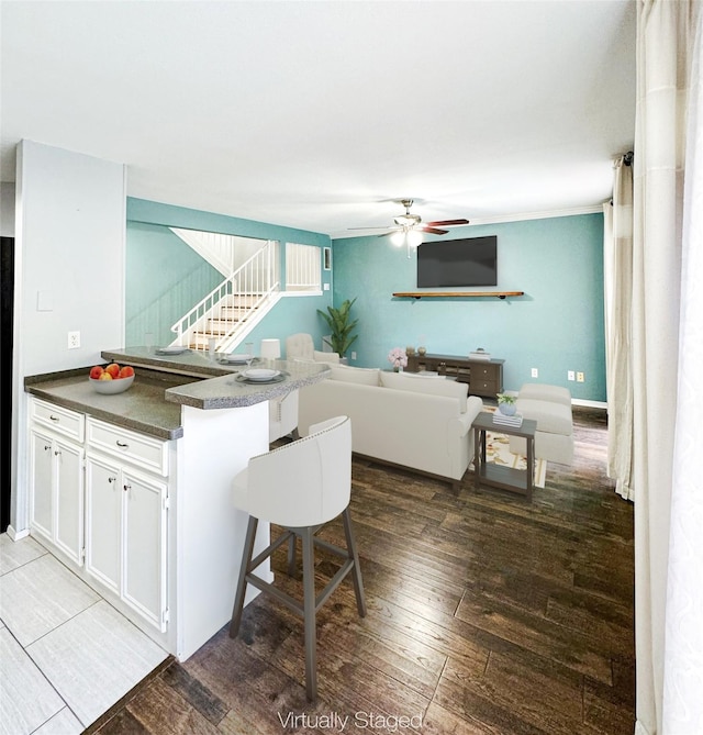 kitchen featuring white cabinets, dark countertops, ceiling fan, wood-type flooring, and a peninsula