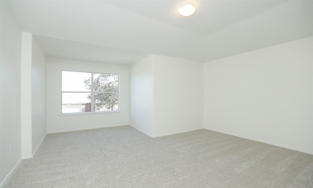 spare room featuring light carpet and baseboards