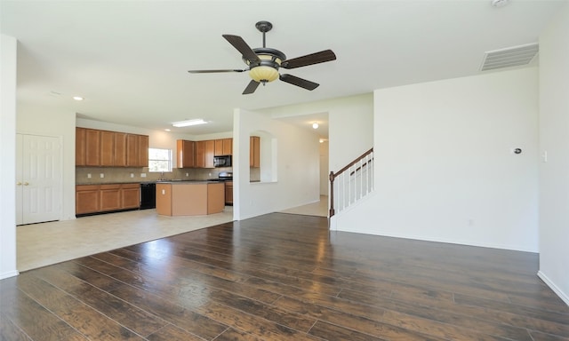 unfurnished living room featuring a ceiling fan, visible vents, stairway, and wood finished floors