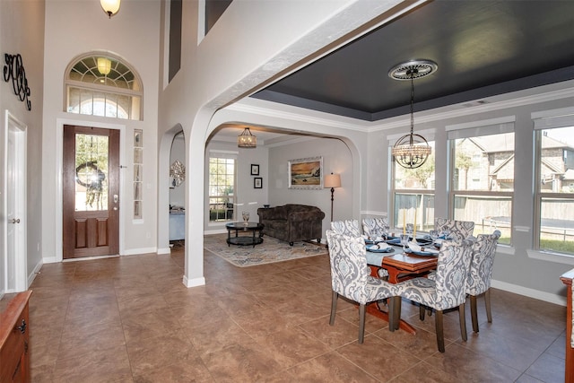 tiled dining room with arched walkways, crown molding, a raised ceiling, an inviting chandelier, and baseboards