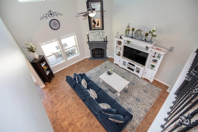 tiled living room with a fireplace with raised hearth, ceiling fan, a high ceiling, and baseboards