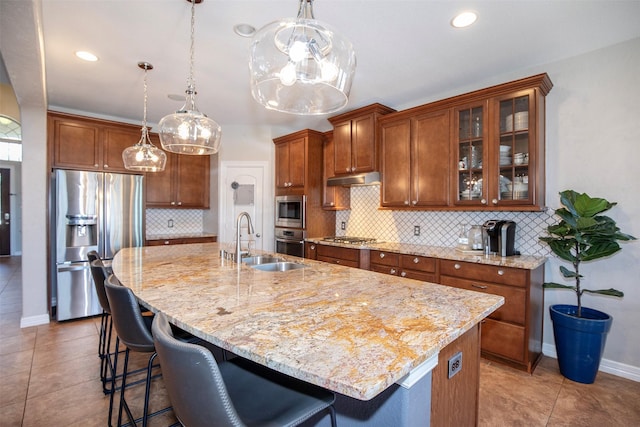 kitchen with brown cabinetry, appliances with stainless steel finishes, a kitchen island with sink, a kitchen bar, and a sink