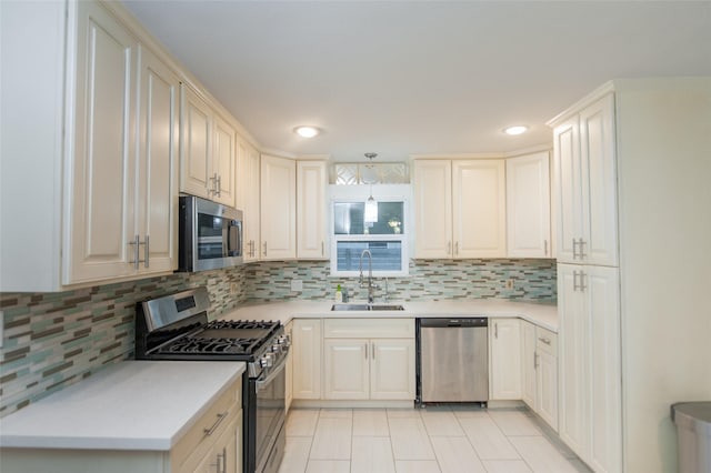 kitchen with a sink, light countertops, appliances with stainless steel finishes, decorative backsplash, and pendant lighting