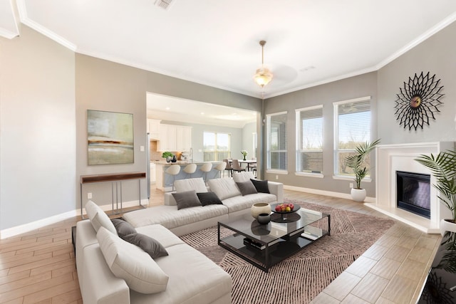 living area with light wood-style floors, a glass covered fireplace, crown molding, and baseboards