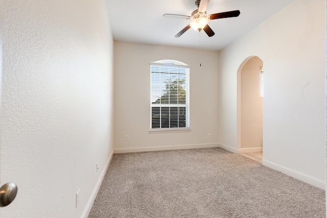 carpeted empty room with ceiling fan, baseboards, and arched walkways