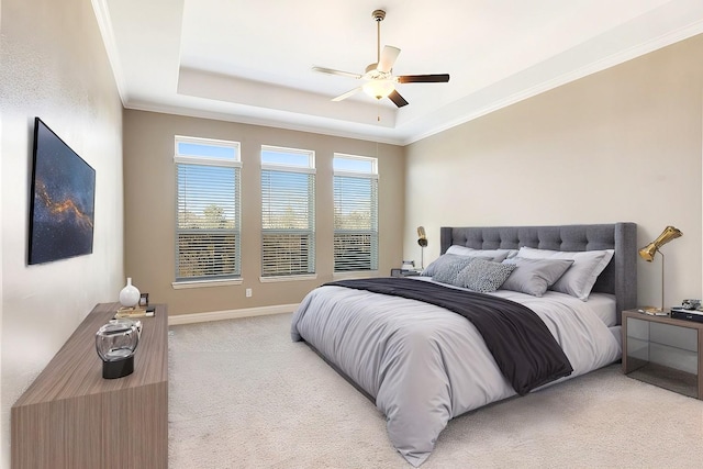 bedroom with light carpet, baseboards, ceiling fan, ornamental molding, and a tray ceiling