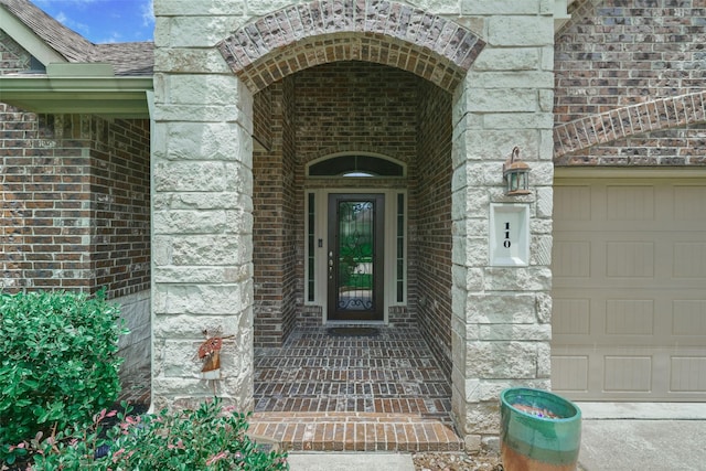 doorway to property with a shingled roof, stone siding, brick siding, and an attached garage