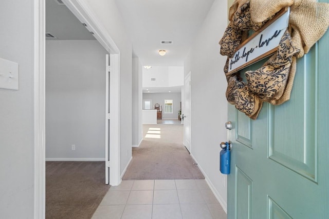 corridor featuring visible vents, light tile patterned flooring, baseboards, and light colored carpet