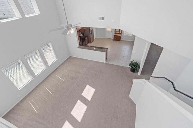 carpeted living area featuring a towering ceiling, tile patterned flooring, visible vents, and ceiling fan