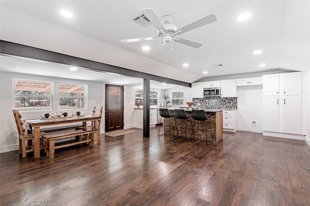 kitchen featuring visible vents, dark wood finished floors, stainless steel microwave, a breakfast bar, and vaulted ceiling