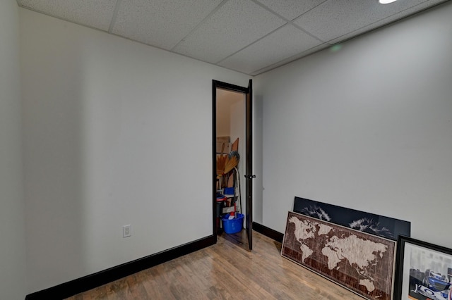 unfurnished bedroom featuring a drop ceiling, baseboards, and wood finished floors