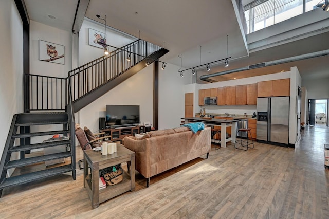 living area with light wood finished floors, stairway, a towering ceiling, and track lighting