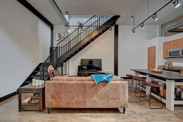 living area with baseboards, light wood-style flooring, stairway, rail lighting, and a high ceiling