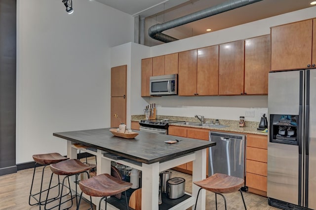 kitchen featuring stainless steel appliances, a sink, light wood-style flooring, and dark stone countertops