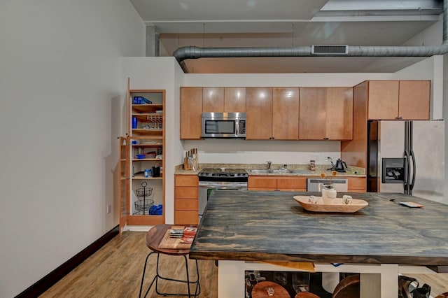 kitchen featuring light wood-style flooring, a sink, visible vents, appliances with stainless steel finishes, and a kitchen bar