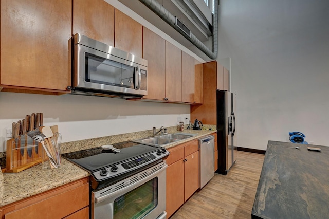 kitchen featuring stainless steel appliances, a towering ceiling, light wood-style floors, a sink, and baseboards